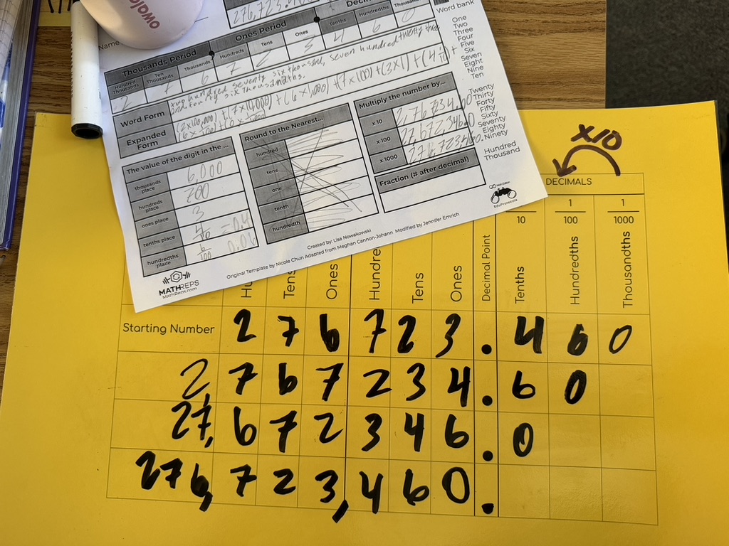 A yellow sheet with a table displaying numbers, including thousands, hundreds, tens, and ones places, with calculations showing various forms of the number 276,734.60.