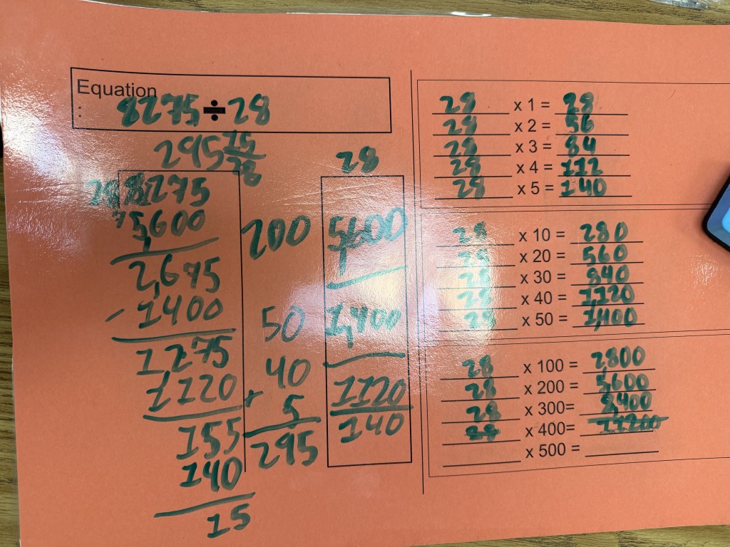 A math worksheet showing division and multiplication problems using the number 28, with calculations and steps outlined in green ink on an orange background.